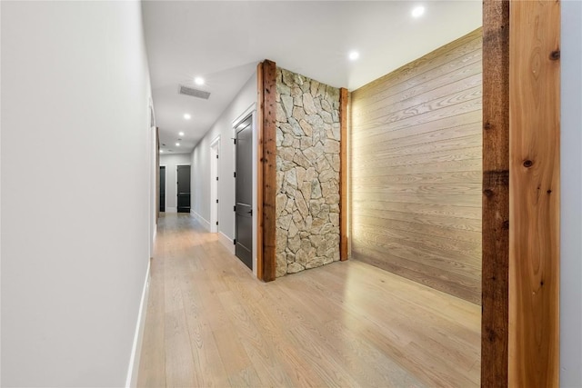 hall featuring light wood-style floors, recessed lighting, visible vents, and wood walls