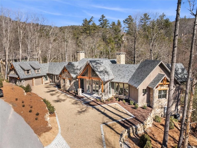 view of front of home featuring dirt driveway, stone siding, a chimney, french doors, and a wooded view