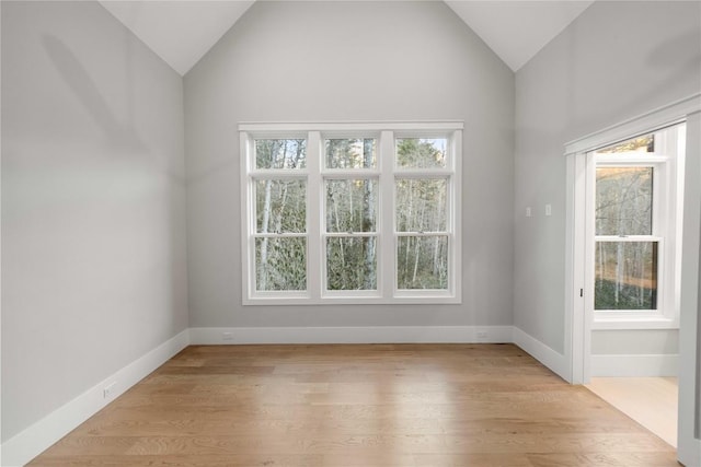 spare room with vaulted ceiling, light wood-style flooring, and baseboards