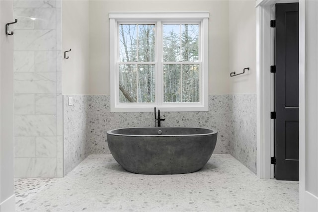 full bathroom with tile walls, a freestanding bath, and wainscoting