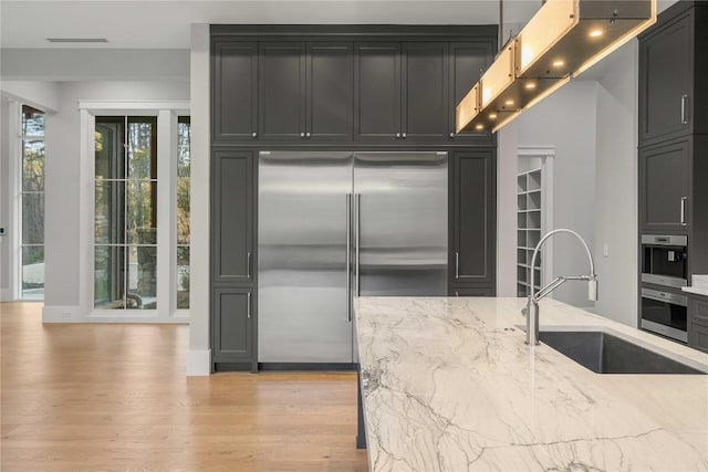 kitchen featuring visible vents, light stone counters, light wood-type flooring, a sink, and built in fridge