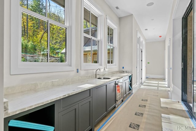 bar with wine cooler, sink, light stone counters, and gray cabinets