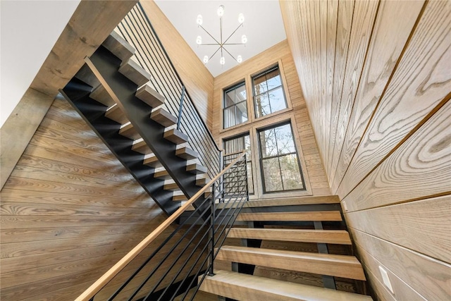 stairs with a high ceiling, wooden walls, and a chandelier