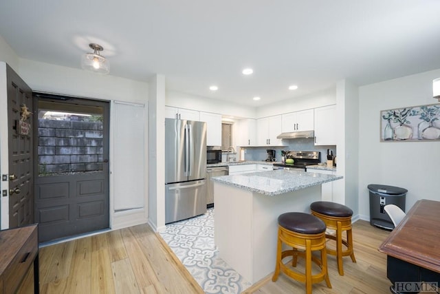 kitchen with light hardwood / wood-style floors, white cabinetry, a breakfast bar area, stainless steel appliances, and light stone counters