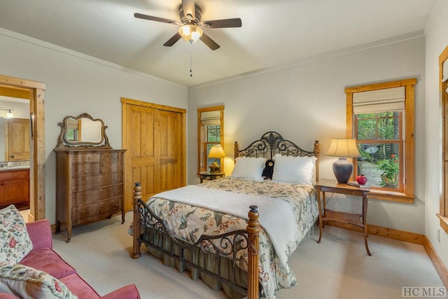 bedroom featuring ornamental molding, light colored carpet, ceiling fan, ensuite bath, and a closet