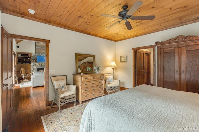 bedroom featuring ceiling fan, dark hardwood / wood-style flooring, a stone fireplace, and wooden ceiling