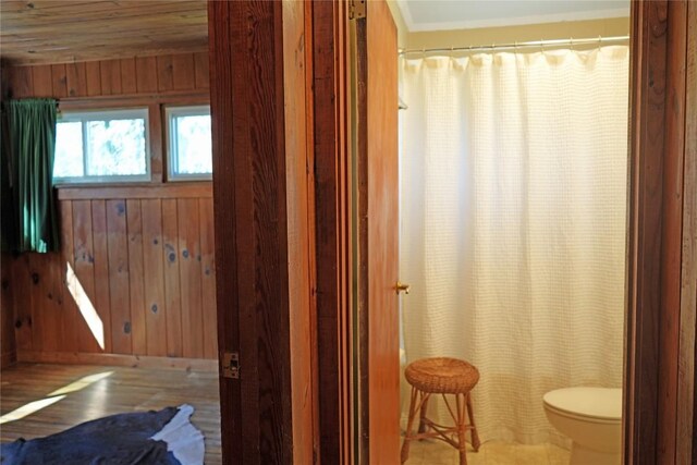 full bath with wooden walls, toilet, a shower with shower curtain, and wood finished floors