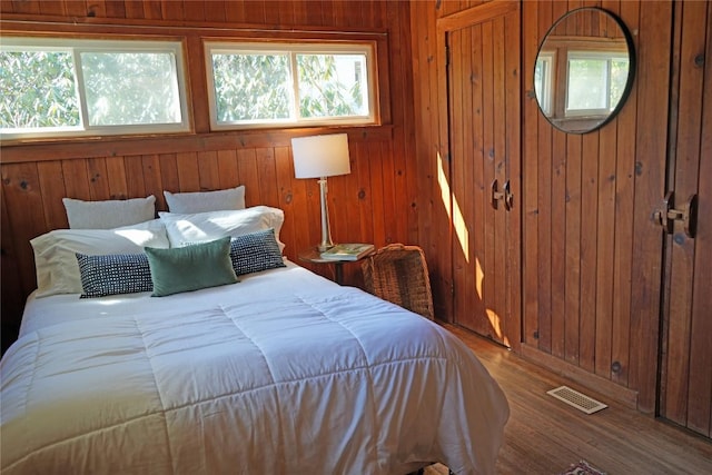 bedroom with visible vents, multiple windows, wooden walls, and wood finished floors