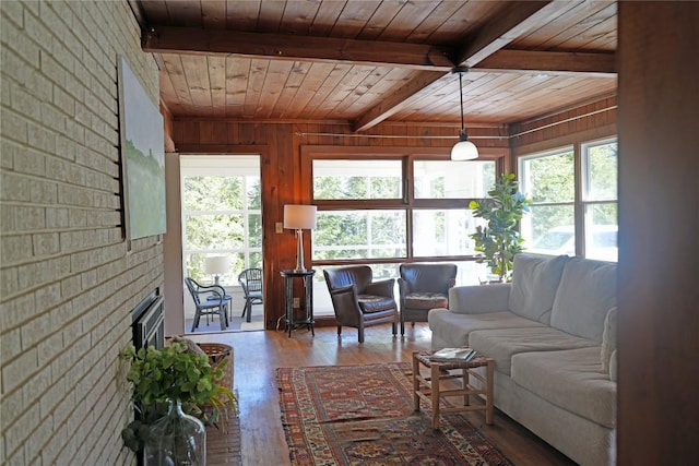 living room featuring beamed ceiling, wood finished floors, wooden ceiling, brick wall, and a brick fireplace