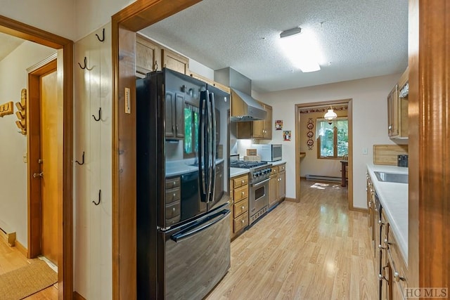 kitchen featuring wall chimney exhaust hood, black fridge, light hardwood / wood-style flooring, stainless steel range, and a baseboard heating unit