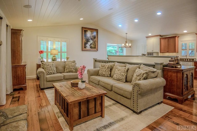 living room featuring lofted ceiling, sink, a chandelier, and light wood-type flooring