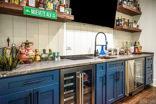 bar with sink, dark wood-type flooring, blue cabinetry, and beverage cooler