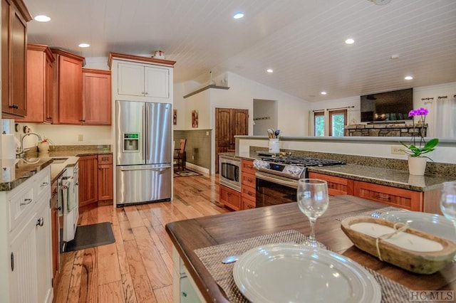 kitchen with lofted ceiling, sink, appliances with stainless steel finishes, dark stone countertops, and light wood-type flooring