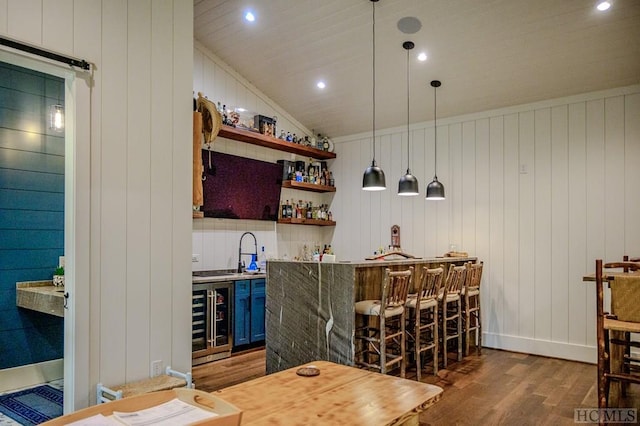 bar with vaulted ceiling, wood-type flooring, wine cooler, hanging light fixtures, and blue cabinetry