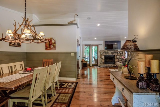 dining area featuring hardwood / wood-style flooring, ornamental molding, a stone fireplace, and a notable chandelier