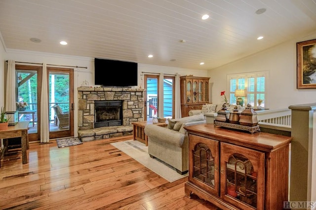 living room featuring lofted ceiling, a stone fireplace, a healthy amount of sunlight, and light wood-type flooring