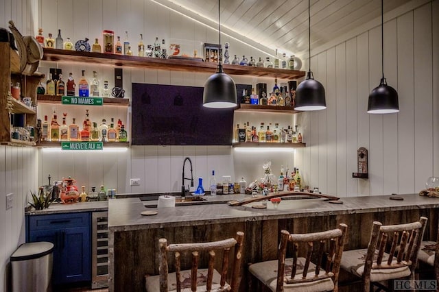 bar featuring pendant lighting, blue cabinetry, vaulted ceiling, beverage cooler, and wood walls