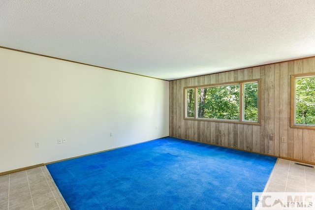 empty room featuring wooden walls, a textured ceiling, and visible vents