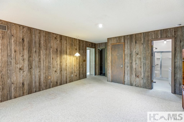 empty room featuring visible vents, wood walls, and carpet
