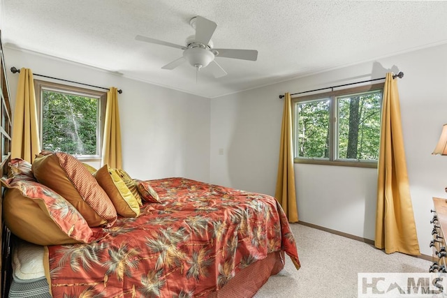 bedroom with a ceiling fan, light carpet, a textured ceiling, and multiple windows