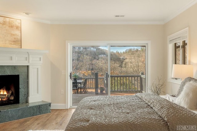 bedroom featuring a premium fireplace, access to outside, crown molding, and light hardwood / wood-style flooring