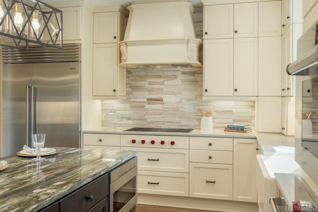 kitchen featuring hanging light fixtures, custom range hood, built in appliances, and decorative backsplash