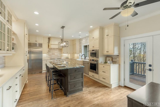 kitchen featuring pendant lighting, appliances with stainless steel finishes, a center island, custom range hood, and a kitchen bar