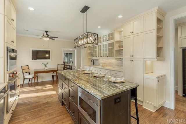 kitchen with hanging light fixtures, light wood-type flooring, a kitchen island, light stone countertops, and decorative backsplash