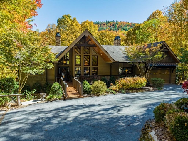 rustic home featuring covered porch, driveway, a chimney, and a garage