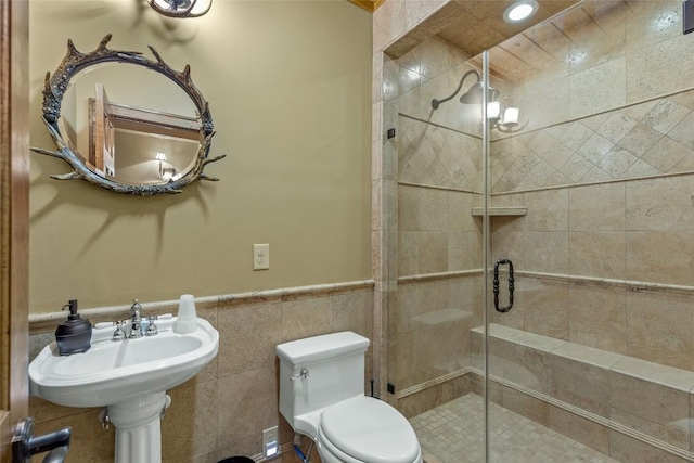 full bathroom featuring wainscoting, a sink, toilet, tile walls, and a stall shower
