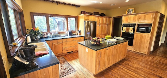 kitchen featuring a sink, light wood-style flooring, a center island, a healthy amount of sunlight, and black appliances