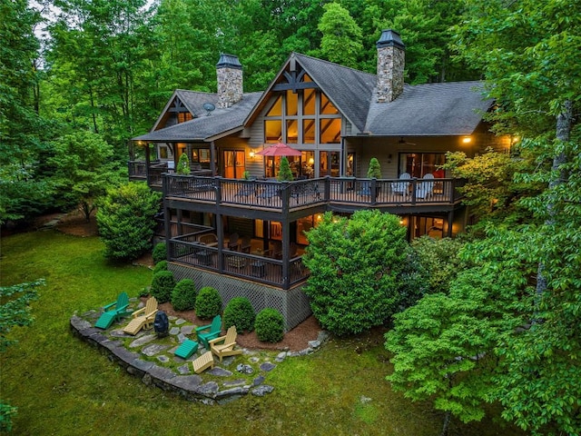back of house with a lawn, a shingled roof, a wooden deck, and a chimney