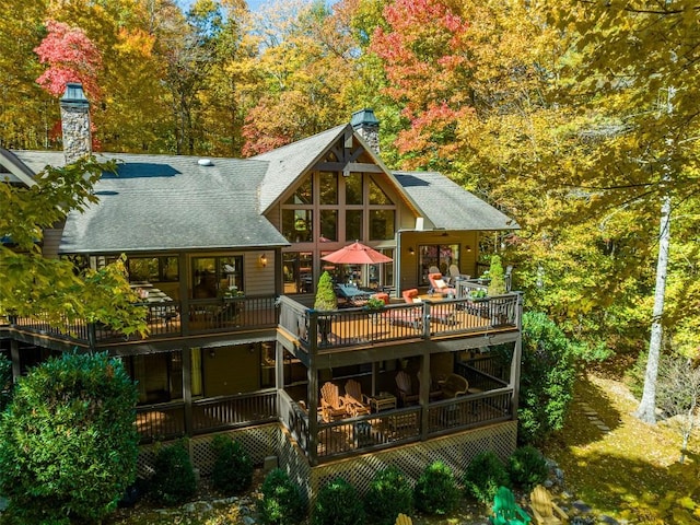 rear view of house with roof with shingles, a wooden deck, and a chimney