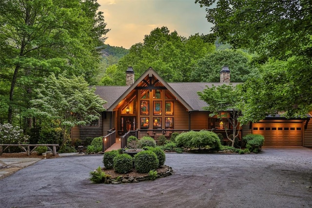 view of front of home with a garage, aphalt driveway, covered porch, a chimney, and a shingled roof