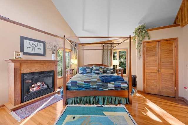 bedroom with baseboards, a glass covered fireplace, wood finished floors, and high vaulted ceiling