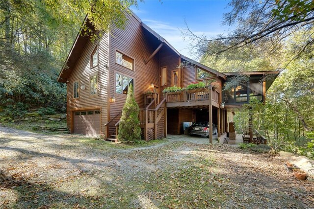 view of side of home with dirt driveway, a deck, stairs, and a garage