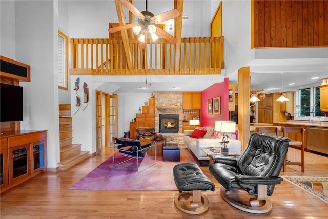 living area featuring a stone fireplace, light wood finished floors, and a towering ceiling