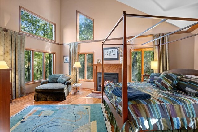 bedroom with a glass covered fireplace, multiple windows, wood finished floors, and a towering ceiling