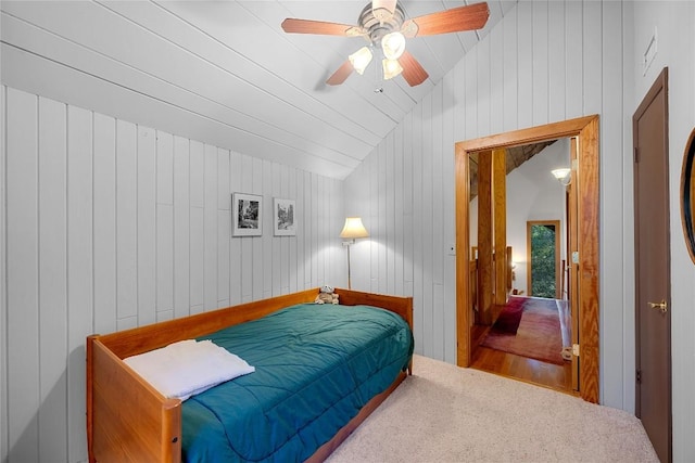 carpeted bedroom with wooden walls, a ceiling fan, and vaulted ceiling