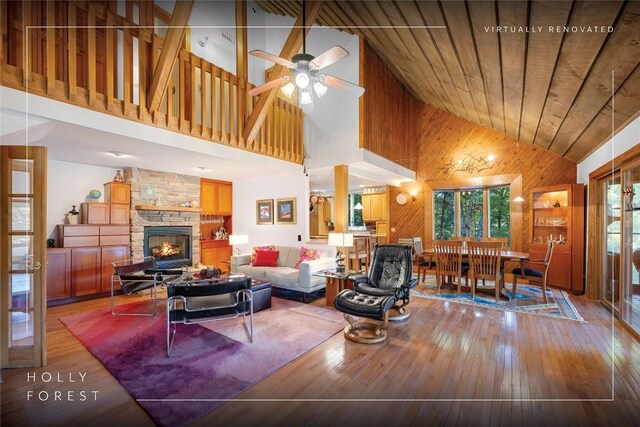 living room with wooden walls, a fireplace, high vaulted ceiling, hardwood / wood-style floors, and a ceiling fan