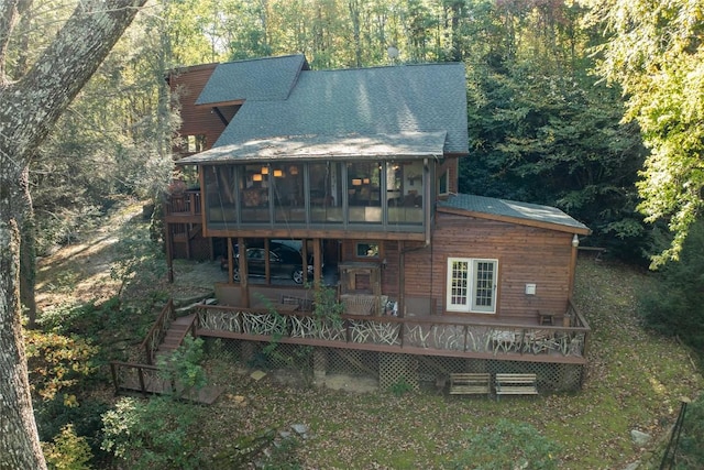 back of house featuring roof with shingles, stairs, a sunroom, a deck, and a wooded view