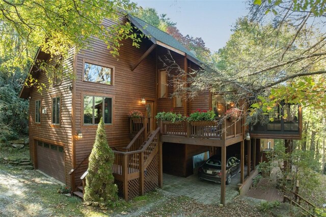 rear view of property featuring an attached garage, stairway, and a deck