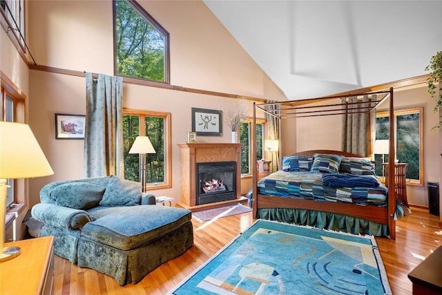 bedroom featuring a glass covered fireplace, wood finished floors, and high vaulted ceiling