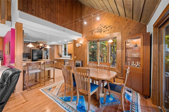 dining room with light wood-style floors, wooden walls, high vaulted ceiling, and wooden ceiling