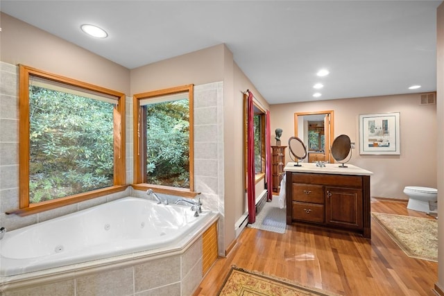 bathroom with visible vents, vanity, wood finished floors, toilet, and a jetted tub