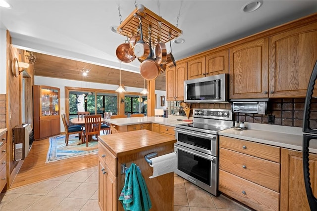 kitchen with decorative backsplash, appliances with stainless steel finishes, light tile patterned floors, a peninsula, and butcher block counters