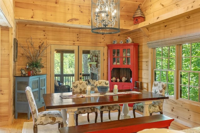 dining room with wood walls, french doors, light wood finished floors, and an inviting chandelier