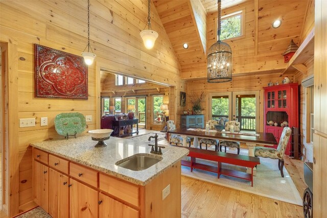 kitchen with high vaulted ceiling, a sink, wooden walls, french doors, and light wood-style flooring