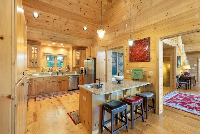 kitchen featuring a peninsula, a sink, light wood-style floors, light stone counters, and appliances with stainless steel finishes