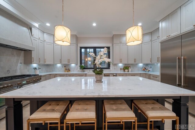 kitchen with appliances with stainless steel finishes, a center island, light stone counters, decorative backsplash, and decorative light fixtures